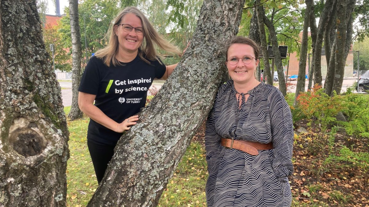 Niina Käyhkö and Sanna Jokela photographed next to a tree in a park-like landscape.