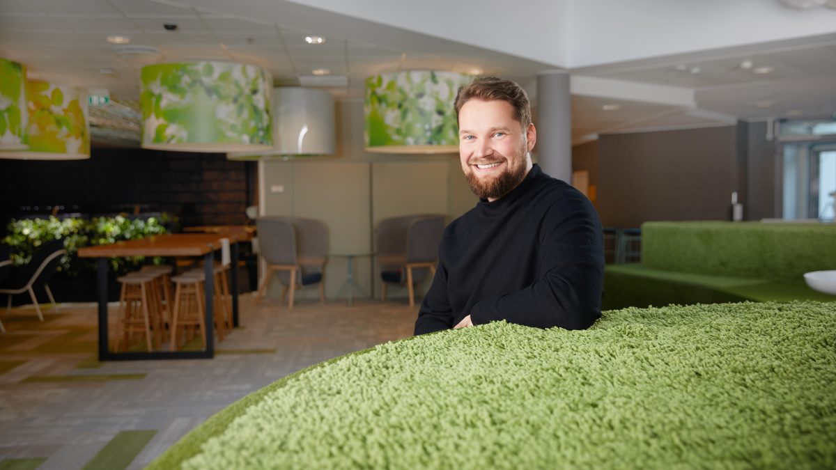 Sami Lankiniemi sits in a spacious office environment, leaning against a grass-green furniture.