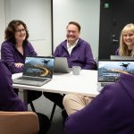 Smiling LIH office staff at the desk wearing purple hoodies.