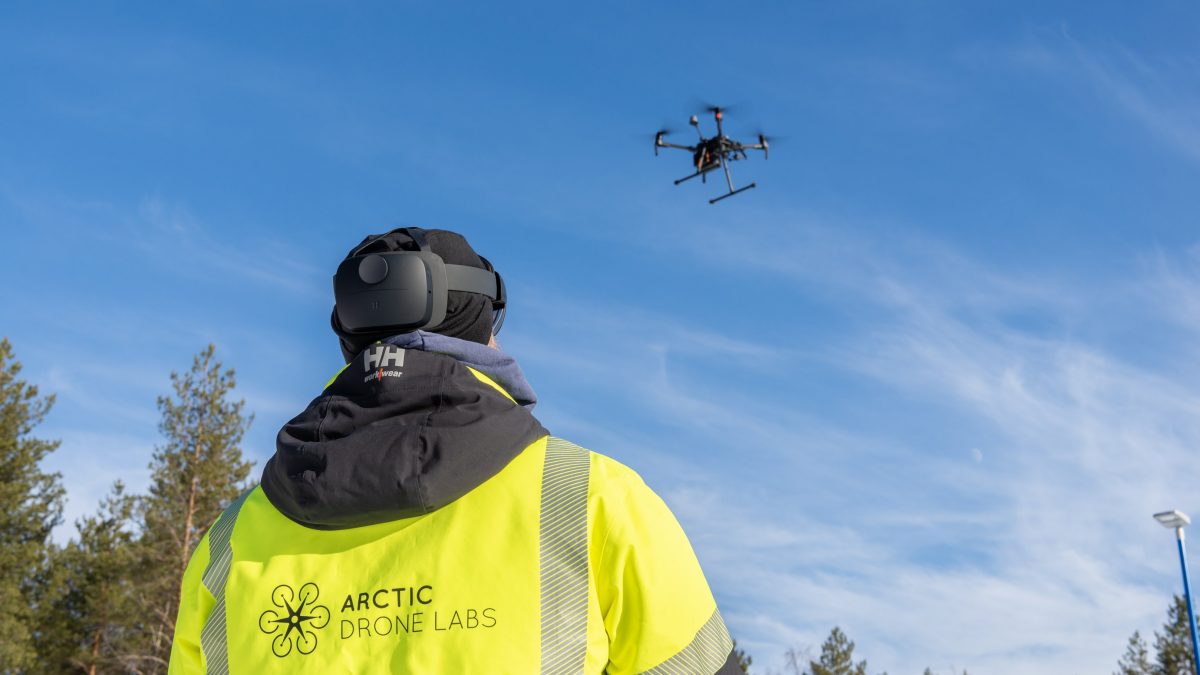 A person flying a drone wearing a jacket that reads Arctic Drone Labs.