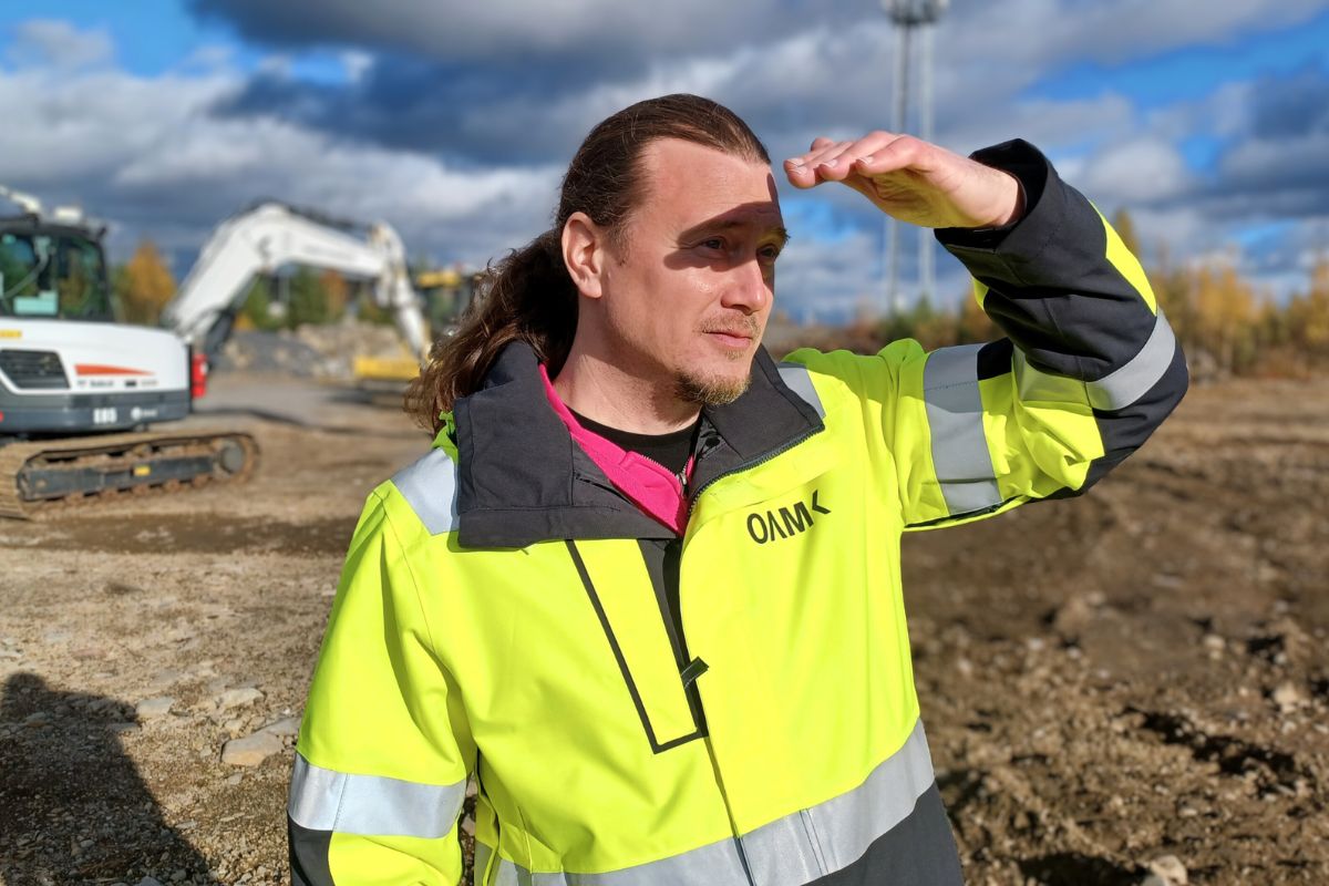 Keltaiseen työtakkiin pukeutunut henkilö tähyilee maisemaa työmaalla.