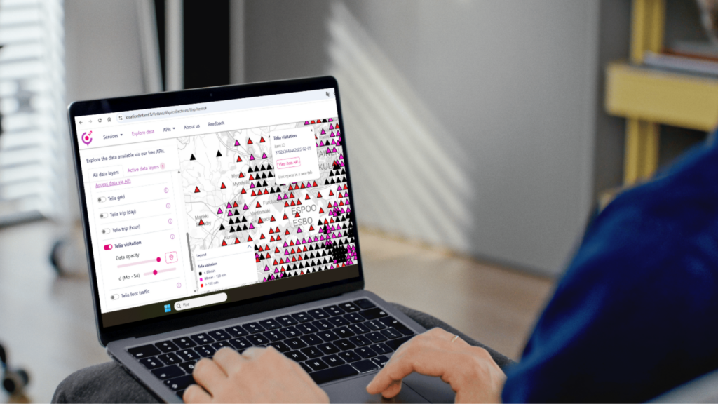 Person using a laptop with a colourful map interface on the screen. The map shows a grid of black and pink triangles and location names such as Espoo. The interface includes options and menus on the left side.