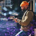 Person standing in an urban street setting, looking at a smartphone, with an abstract digital network overlay representing data connectivity.